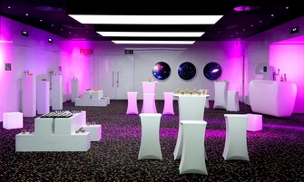 A modern hotel lobby with white furniture, a central bar area, and three wall-mounted galaxy-themed decorations.