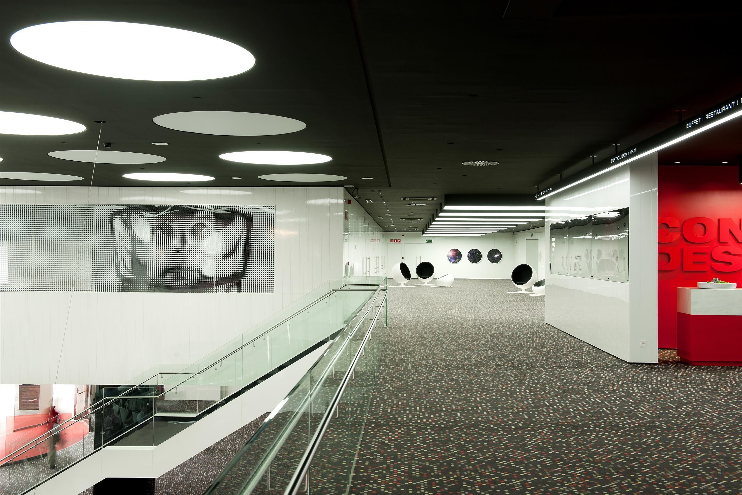 A modern interior with a glass railing, a digital display, and a red accent wall.