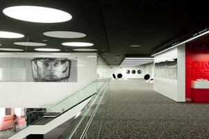 A modern interior with a glass railing, a digital display, and a red accent wall.