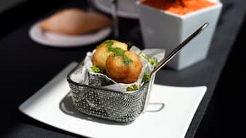 A basket of food items on a table with a wine glass and a bowl of sauce in the background.