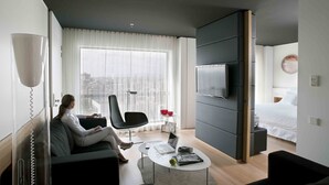Una habitación de hotel moderna con un ventanal grande, un televisor de pantalla plana, un sofá, una mesa de centro y una cama.
