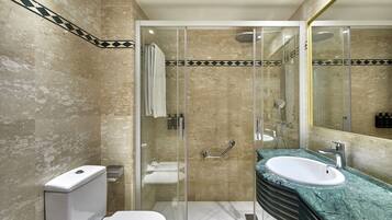 Un baño con ducha de vidrio, inodoro blanco y lavamanos con encimera de mármol verde.