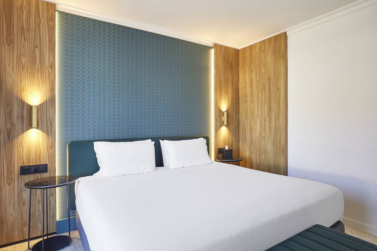 A neatly made bed with white linens, a wooden headboard, and two bedside lamps.