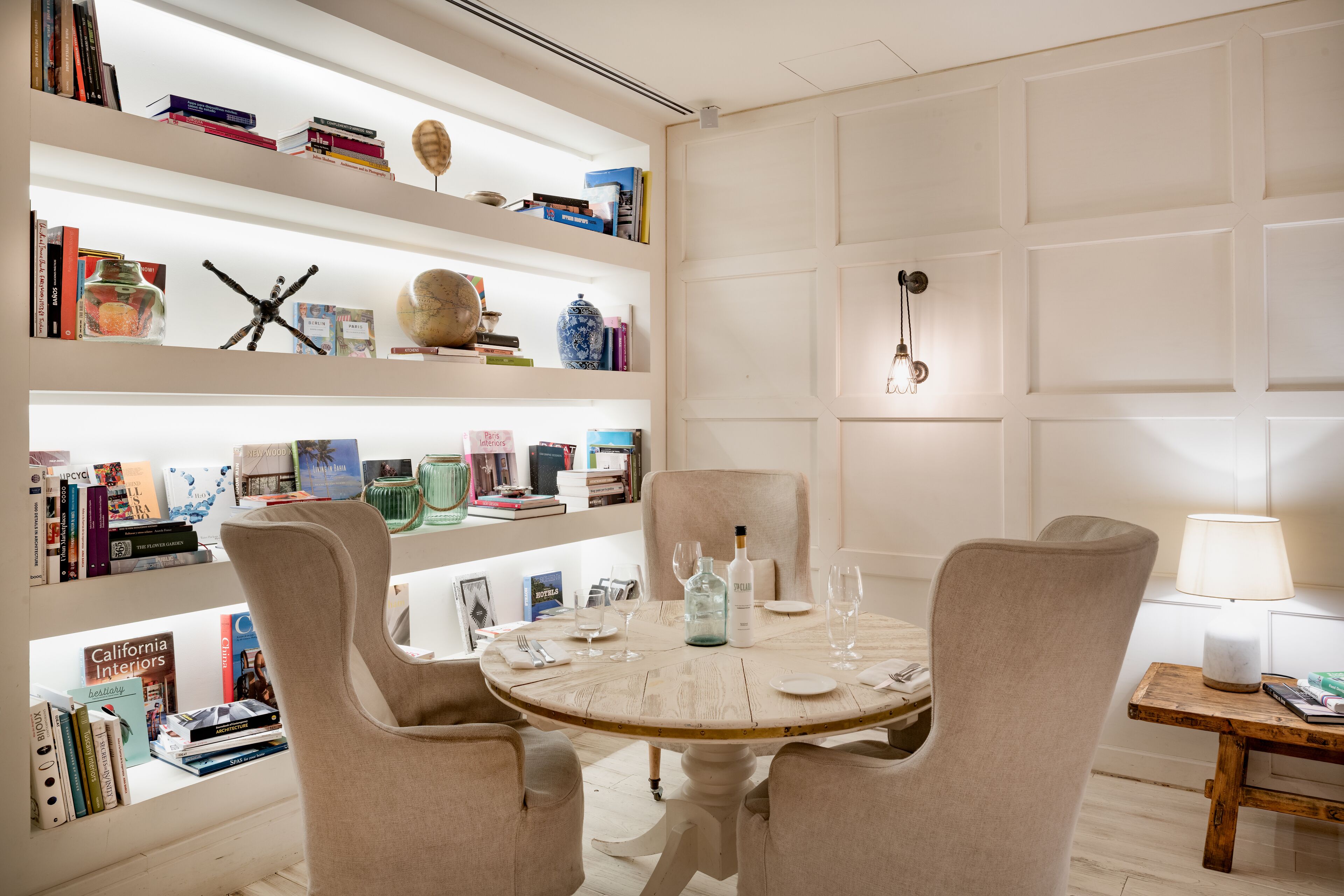 Un coin repas comprenant une table ronde, quatre chaises et une bibliothèque remplie de livres et d’objets décoratifs.
