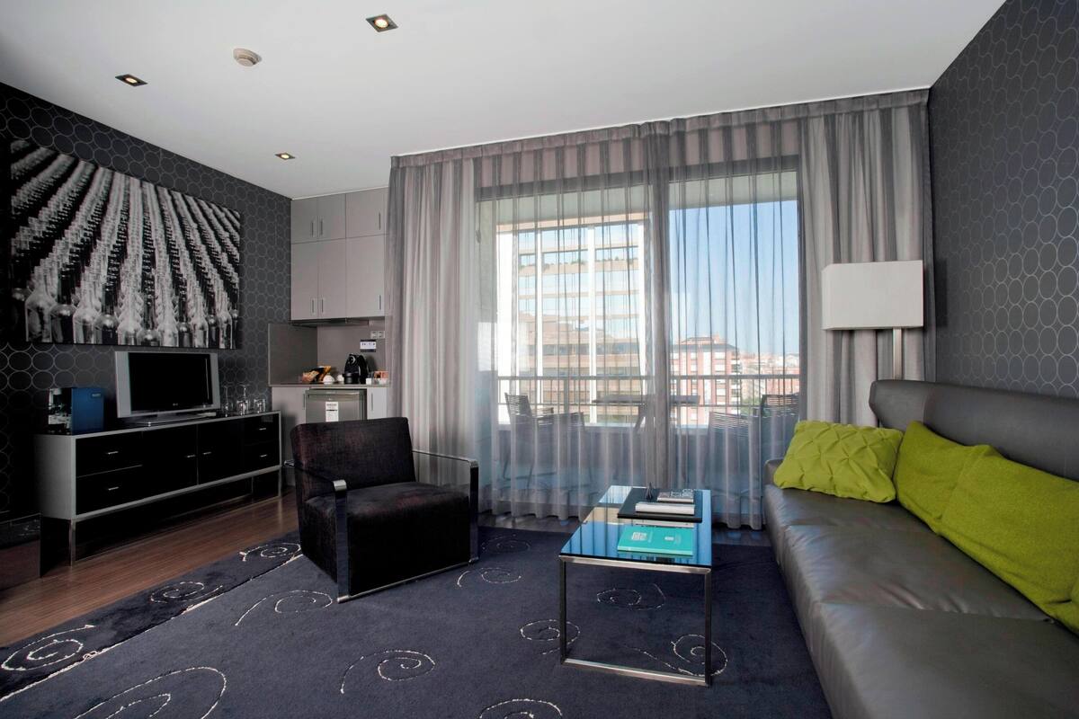 A modern living room with a sofa, a coffee table, a TV, and a large window with curtains.