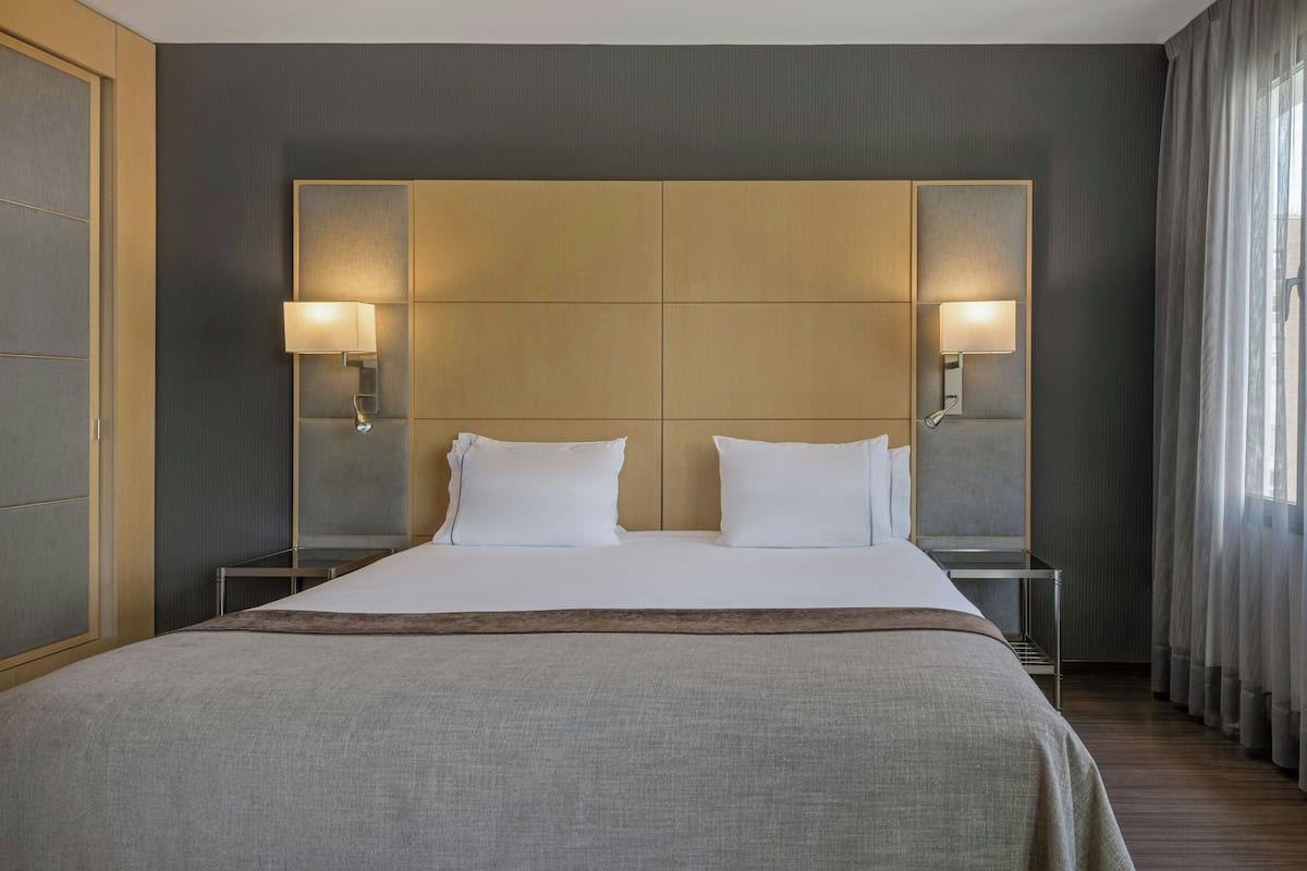 A hotel room with a large bed, two bedside lamps, and a headboard with integrated lighting.