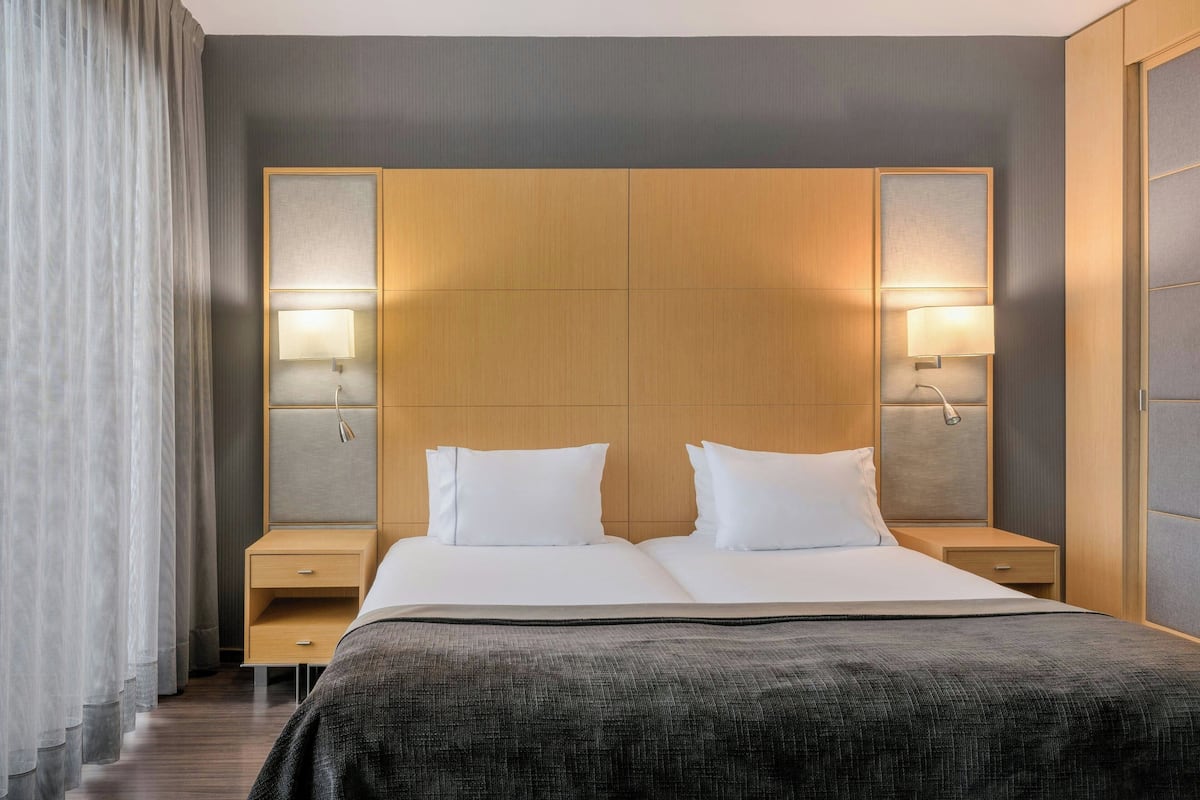 A hotel room with a large bed, two bedside tables, and a headboard with integrated lighting.