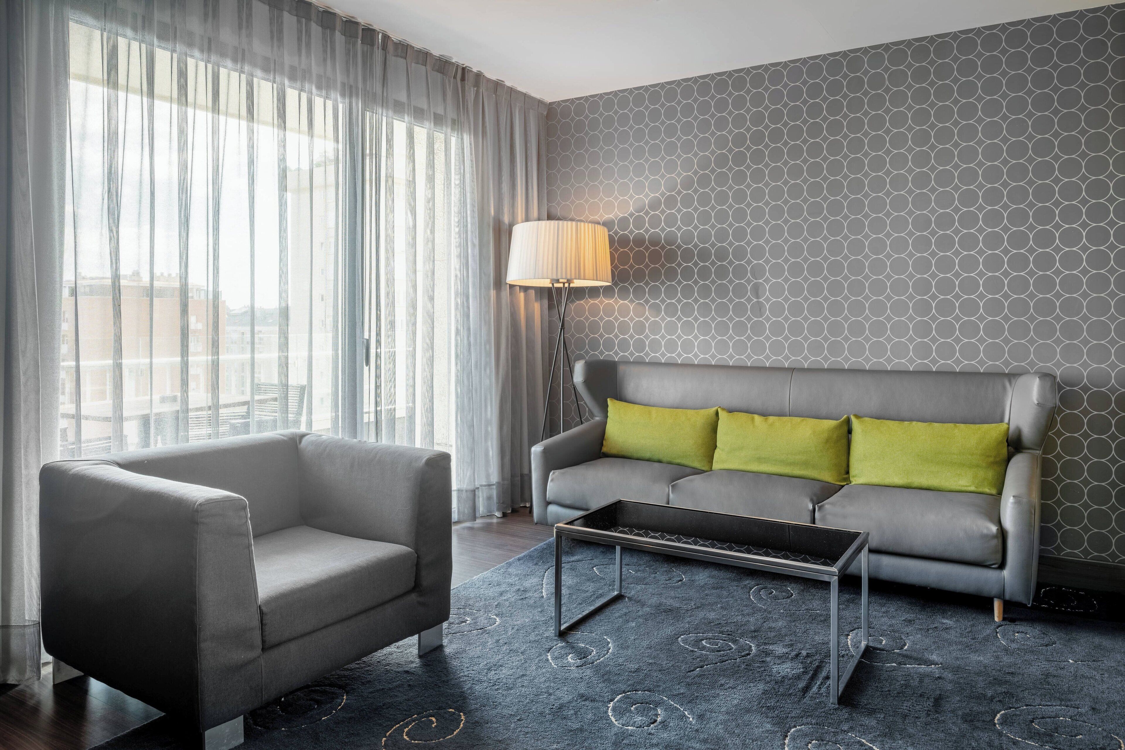A modern living room with a grey sofa, a grey armchair, a patterned rug, and a floor lamp.