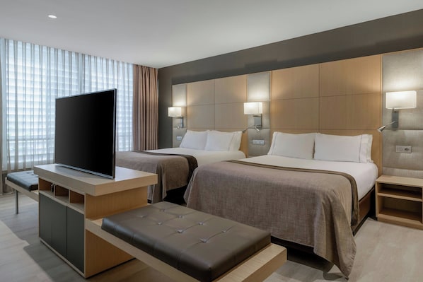A hotel room with two beds, a TV, and a desk. - AC Hotel Victoria Suites by Marriott (Barcelona)