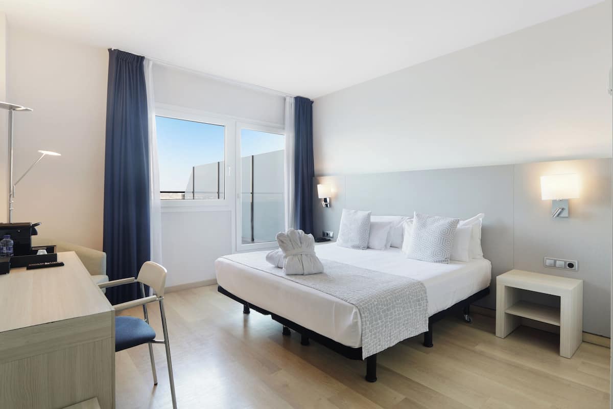 Quarto de hotel com cama, mesas de cabeceira, escrivaninha e uma cadeira.