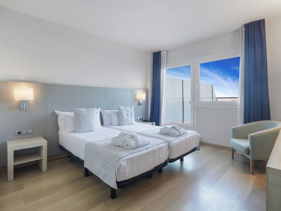 Une chambre d’hôtel avec deux lits, une petite table de chevet, une chaise, un bureau et une fenêtre donnant sur un paysage agréable.