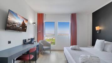 Ein Hotelzimmer mit Bett, Schreibtisch, Stuhl und einem großen Fenster mit Vorhängen.