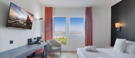 Habitación de hotel con cama, escritorio, silla y un ventanal con cortinas.