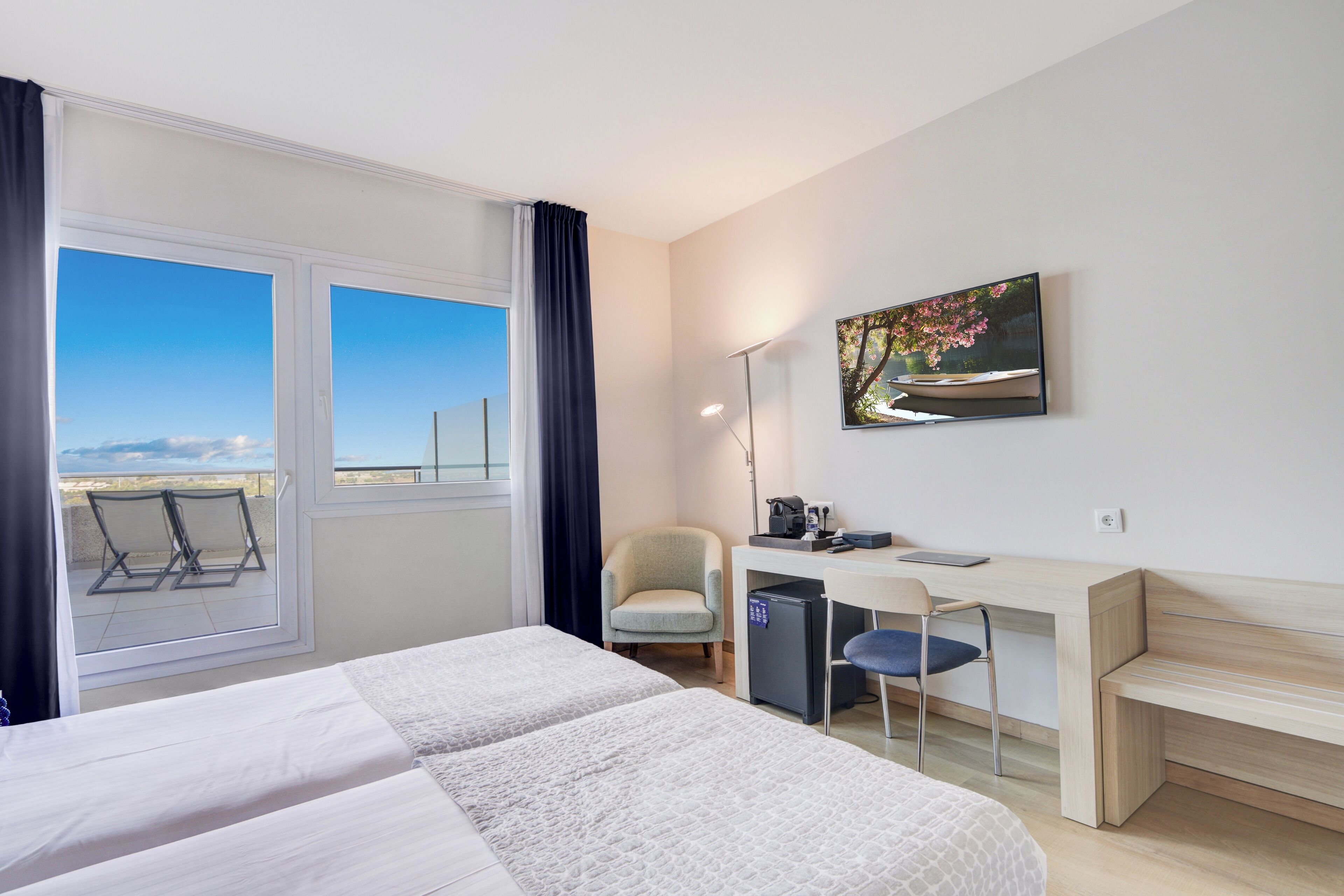 Habitación de hotel con cama, escritorio, silla y vistas al exterior.