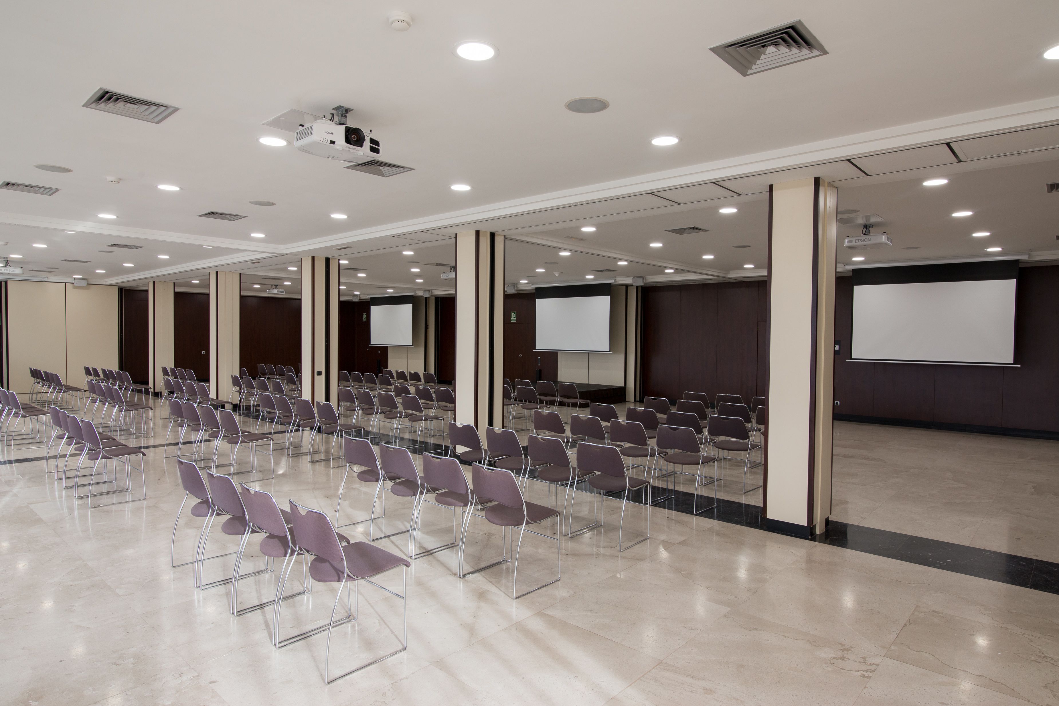 Un salón de conferencias con filas de sillas, un proyector y una pantalla.