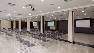 Un salón de conferencias con filas de sillas, un proyector y una pantalla.