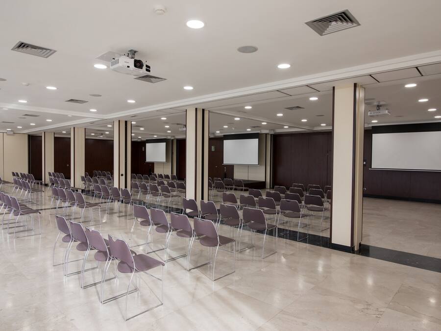 Un salón de conferencias con filas de sillas, un proyector y una pantalla.
