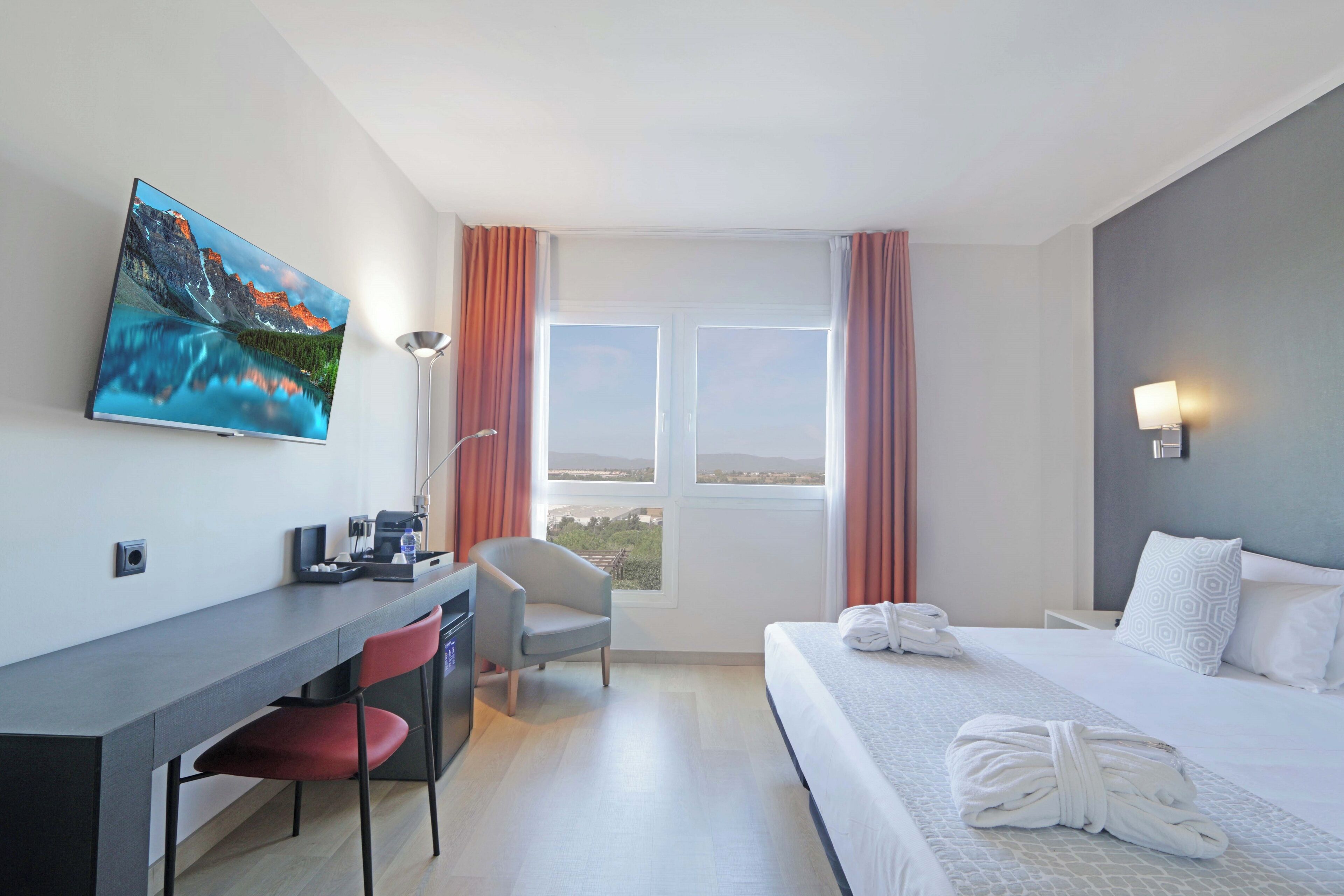 A hotel room with a bed, a desk, a chair, a television, and a window with curtains.