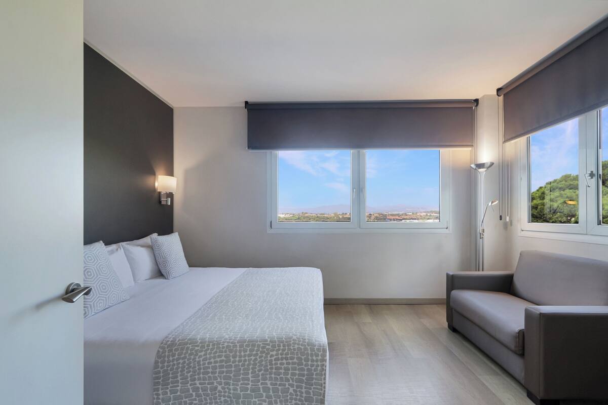Quarto moderno com uma cama grande, um sofá e uma janela com vista para a cidade.