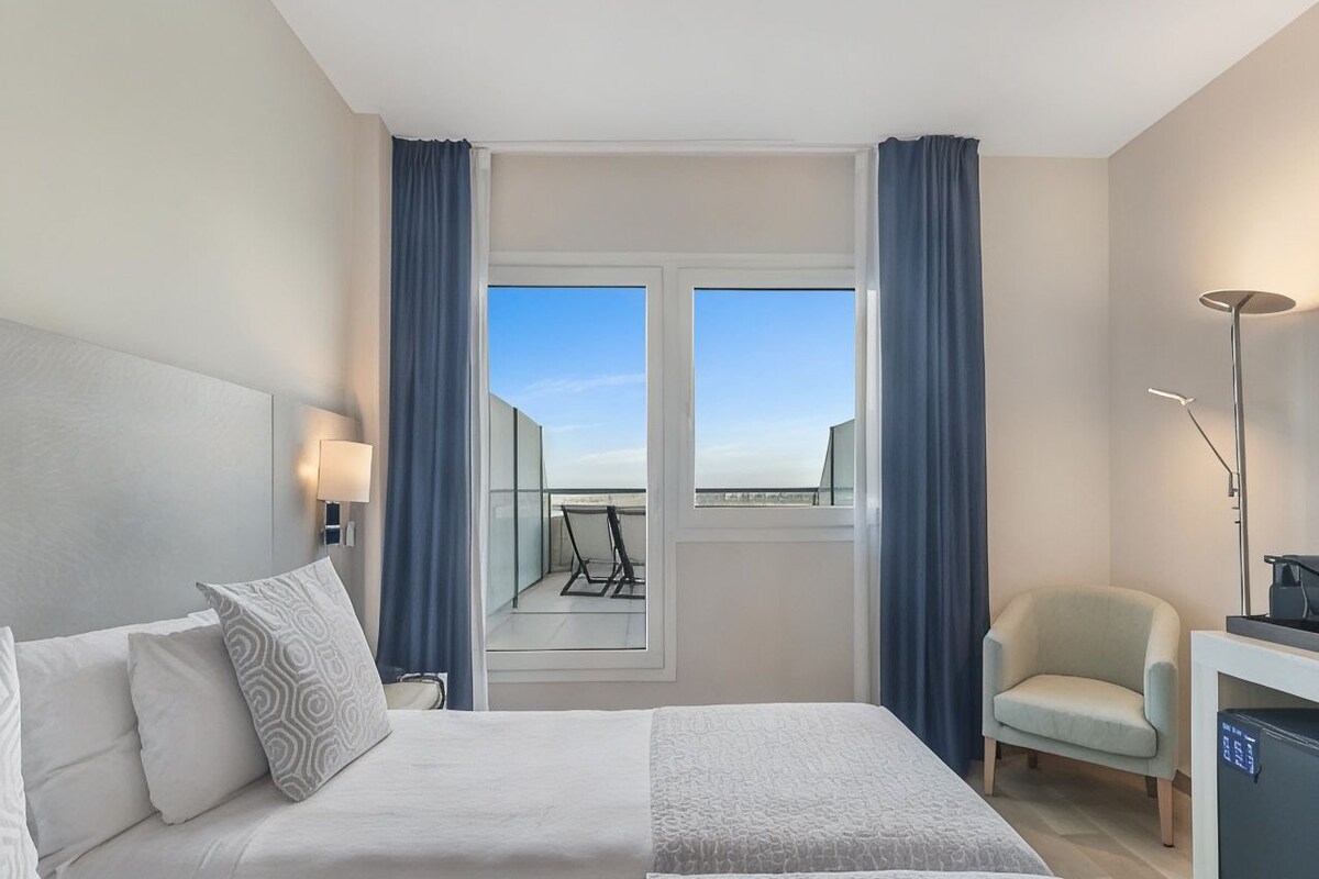 Habitación de hotel con cama, una silla, un escritorio y vistas al exterior.