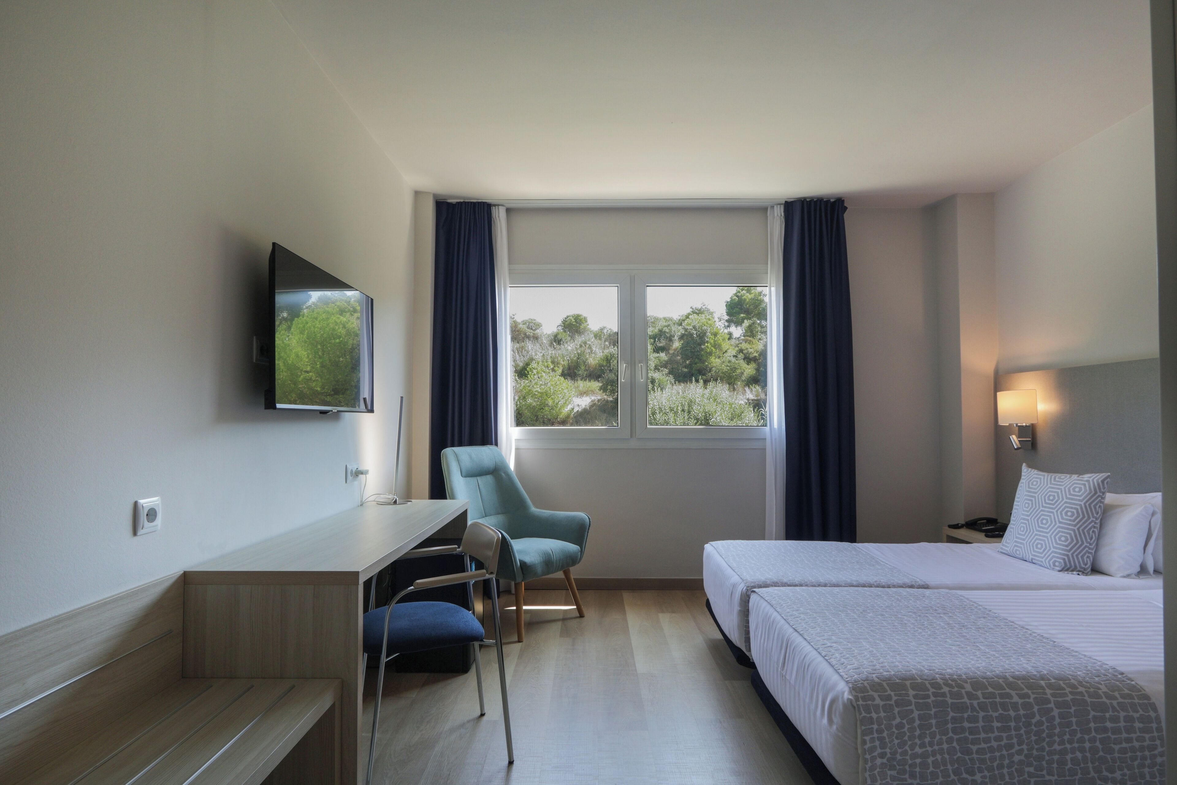 Una habitación de hotel con cama, escritorio, silla y televisor en la pared.