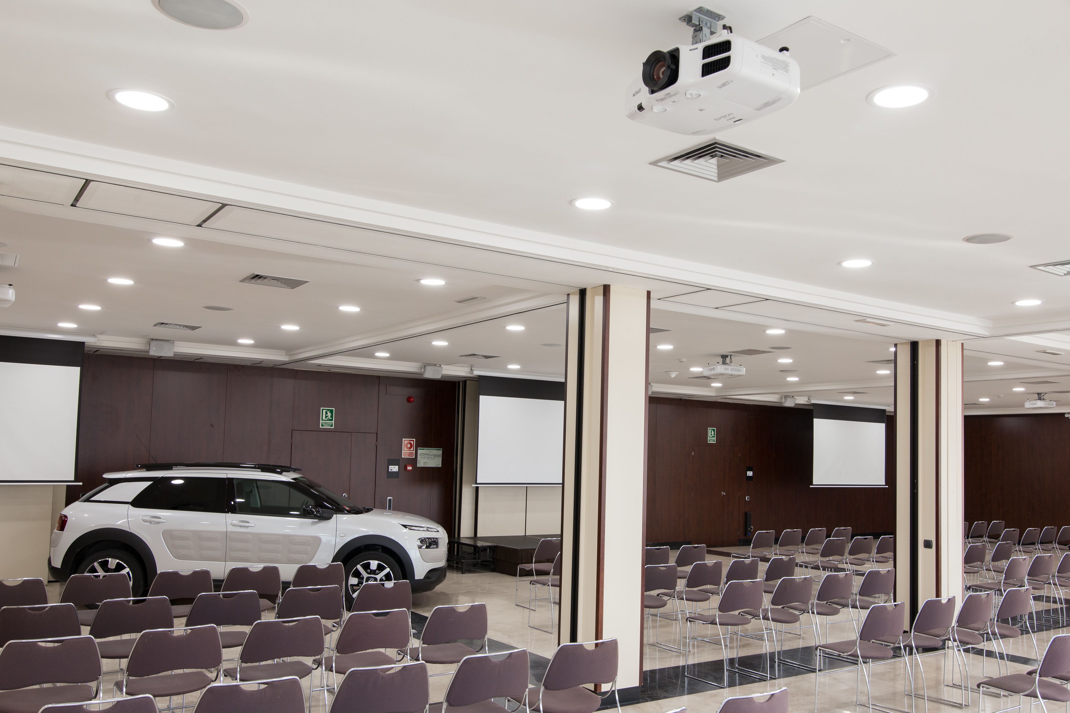 A conference room with rows of chairs, a white SUV, and a projector mounted on the ceiling.