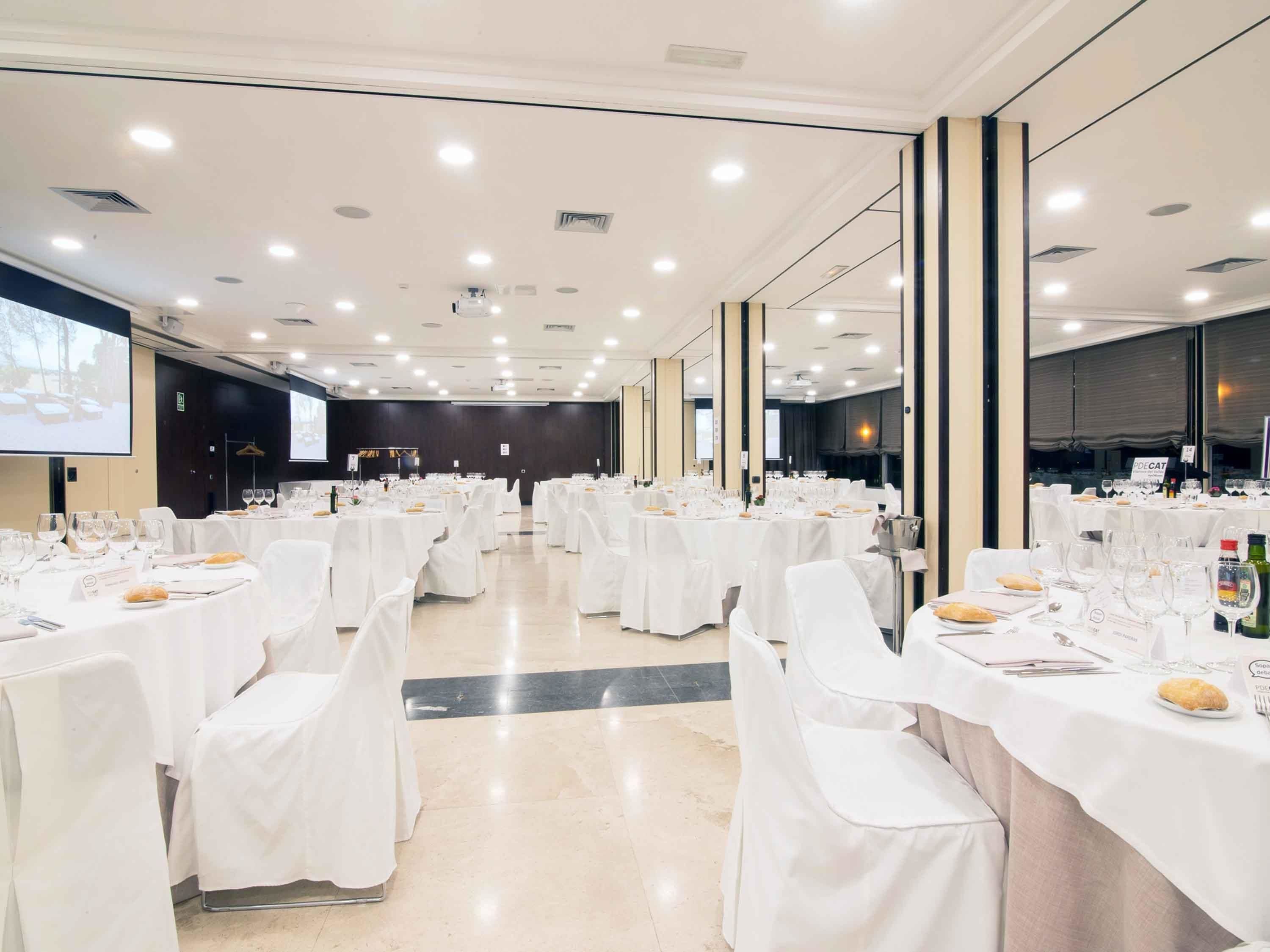 Un salón de conferencias amplio con mesas redondas, manteles blancos y sillas.