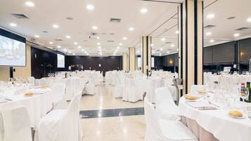 Un salón de conferencias amplio con mesas redondas, manteles blancos y sillas.