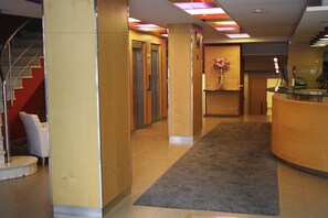 A hotel lobby with a reception desk, a staircase, and a reception area with a vase of flowers. - Hotel Abbot (Barcelona)