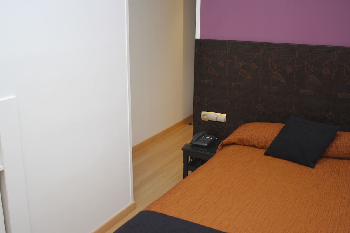 Quarto de hotel com cama, mesa de cabeceira, telefone e parede com padrão geométrico.