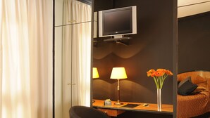A hotel room with a desk, chair, TV, lamp, flowers, and a sofa. - Hotel Abbot (Barcelona)