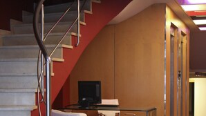 A modern interior with a curved staircase, a flat-screen TV, and a seating area with white chairs. - Hotel Abbot (Barcelona)