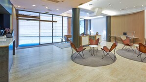 A modern hotel lobby with a reception desk, seating area, and large windows offering a view. - NH Bilbao Deusto (Bilbao)