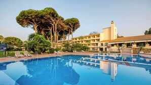A swimming pool with lounge chairs and a building with a tower in the background. - AZZ Guadacorte Campo de Gibraltar (Los Barrios)