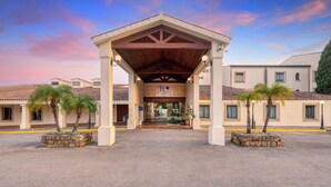 A hotel entrance with a covered patio, palm trees, and a clear sky. - AZZ Guadacorte Campo de Gibraltar (Los Barrios)
