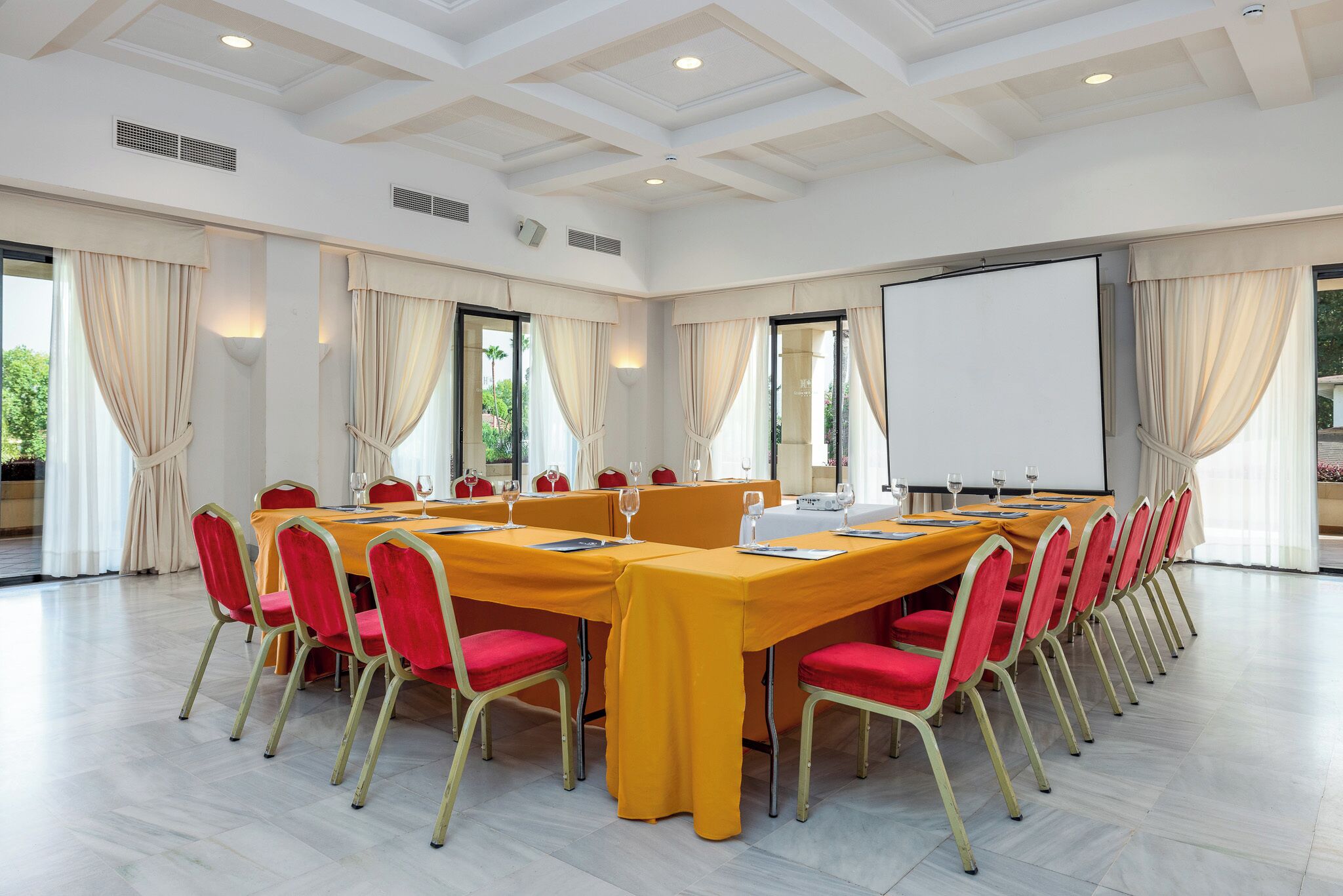 Un salón de conferencias con una larga mesa, sillas rojas y una pizarra.