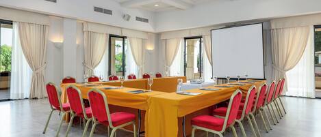 Un salón de conferencias con una larga mesa, sillas rojas y una pizarra.