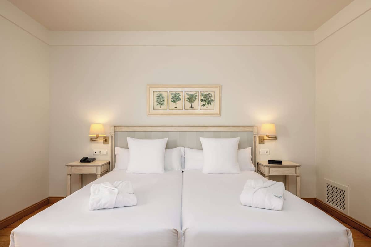A double bed with white linens, two bedside tables with lamps, and a framed botanical print above the bed.