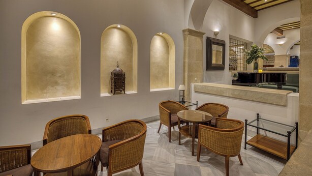 A dining area with wicker chairs and a round table, arched windows, and a stone column. - AZZ Guadacorte Campo de Gibraltar (Los Barrios)