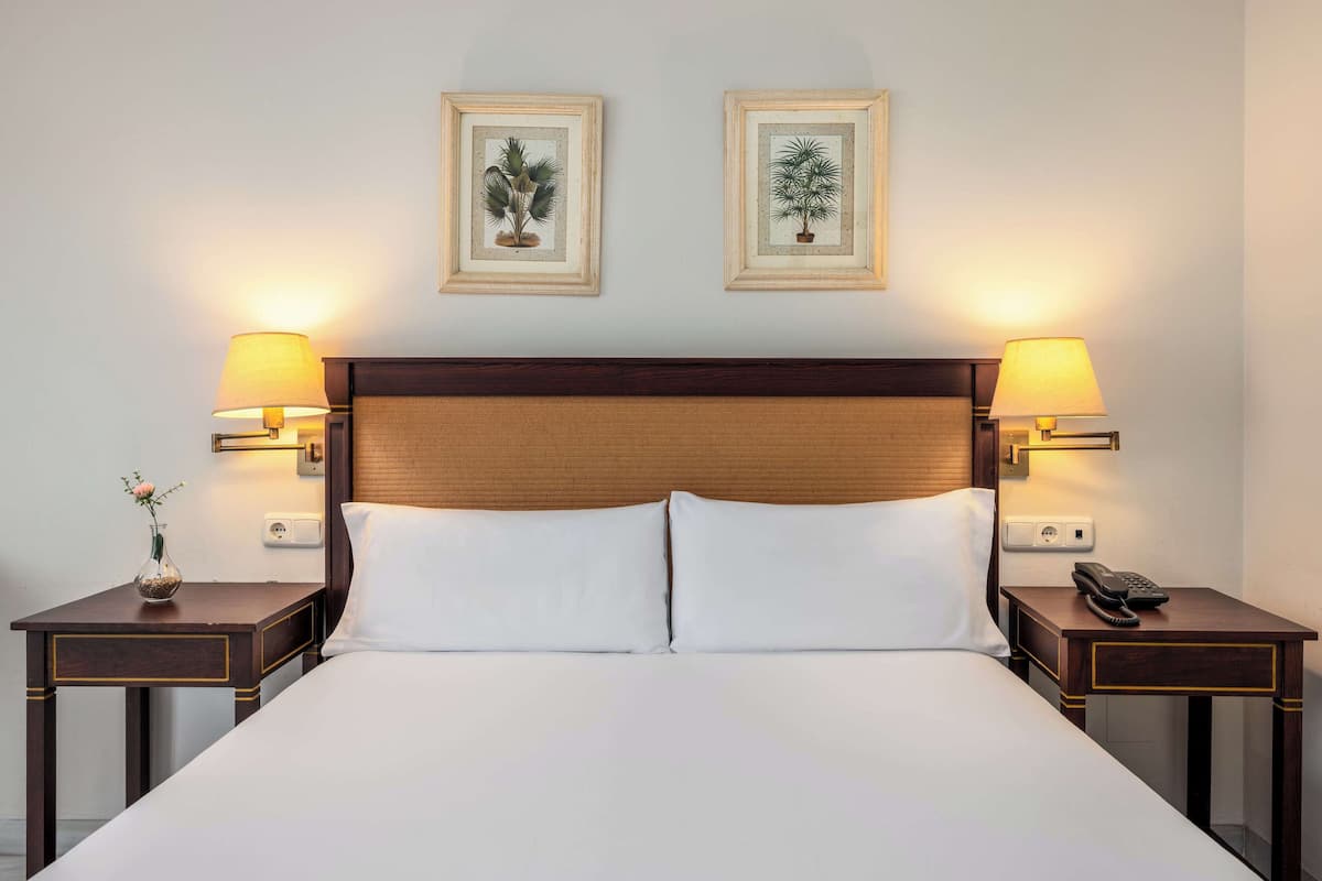 A hotel room with a large bed, two bedside tables with lamps, and two framed botanical prints on the wall.