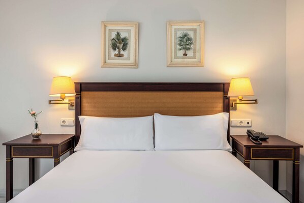 A hotel room with a large bed, two bedside tables with lamps, and two framed botanical prints on the wall. - AZZ Guadacorte Campo de Gibraltar (Los Barrios)