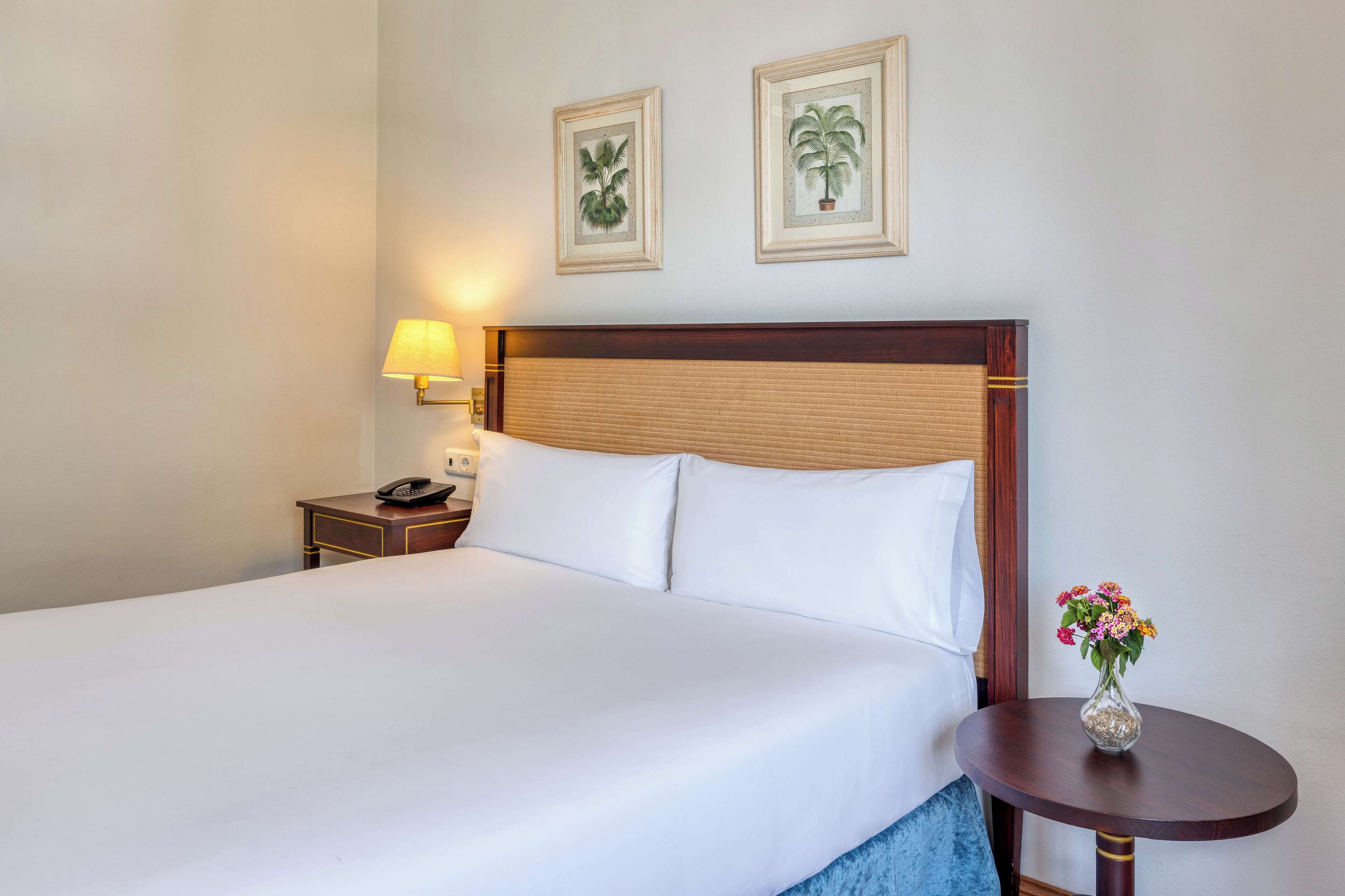 Habitación de hotel con una cama grande, una mesita de noche con lámpara y dos cuadros en la pared.