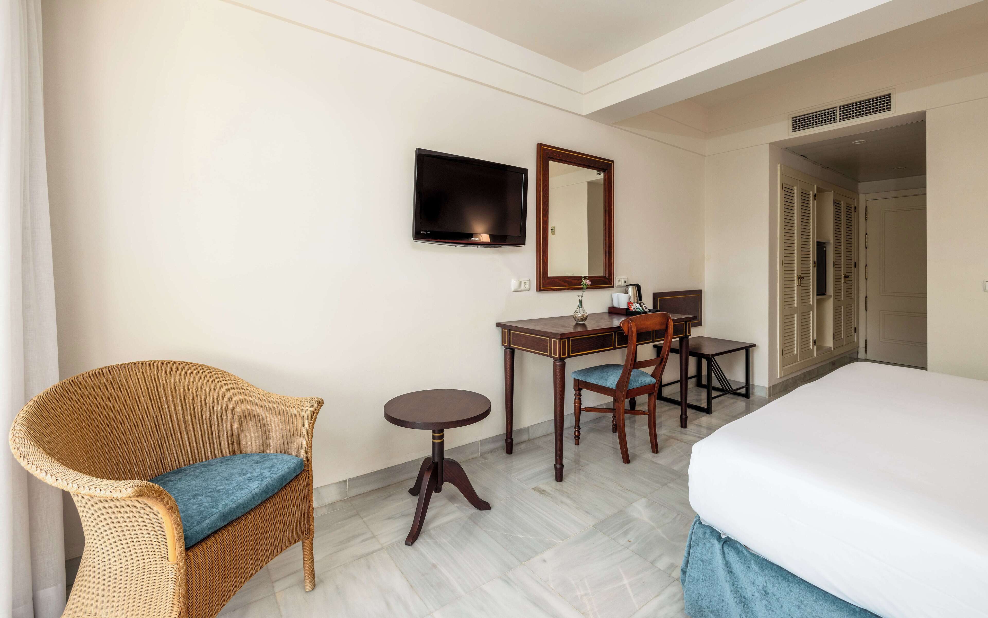 Una habitación de hotel con una cama, un escritorio con silla, televisión y espejo.