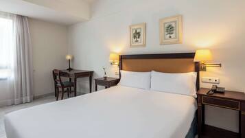 Ein Hotelzimmer mit einem großen Bett, einem Schreibtisch, zwei Nachttischlampen und zwei gerahmten Bildern an der Wand.
