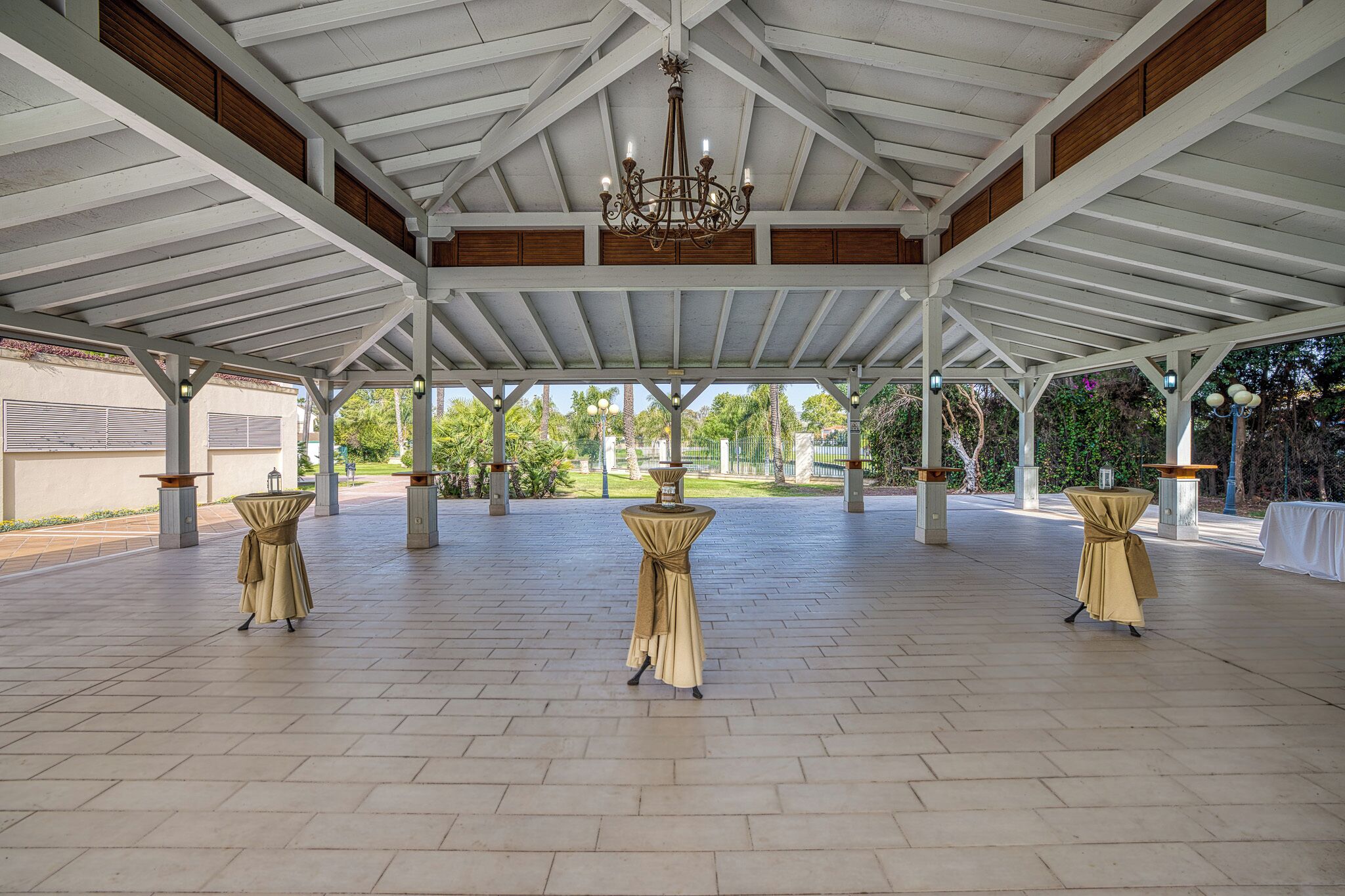 An open pavilion with a high ceiling and a chandelier. Tables are covered with beige tablecloths.