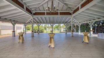 An open pavilion with a high ceiling and a chandelier. Tables are covered with beige tablecloths.