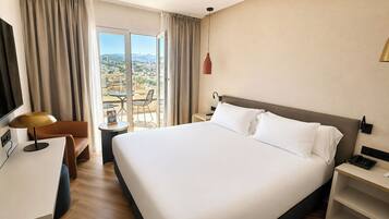 Una habitación de hotel con una cama grande, un escritorio, una silla, un televisor y vistas a la ciudad.
