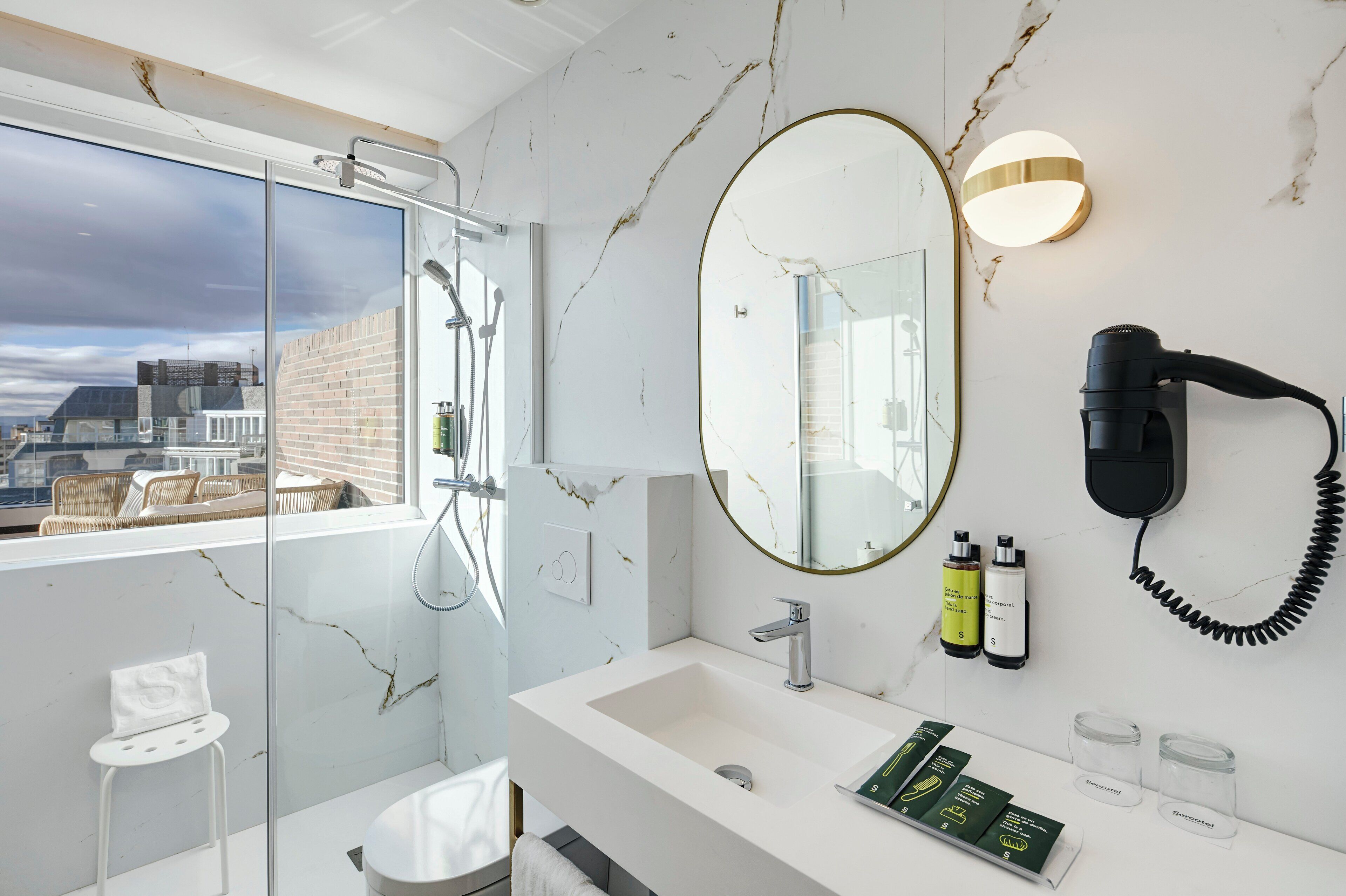 Un baño moderno con un ventanal amplio, un lavabo blanco, un espejo y un secador de pelo montado en la pared.