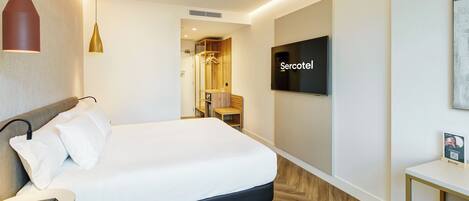 Ett modernt hotellrum med en säng, en TV, ett litet bord och en stol.