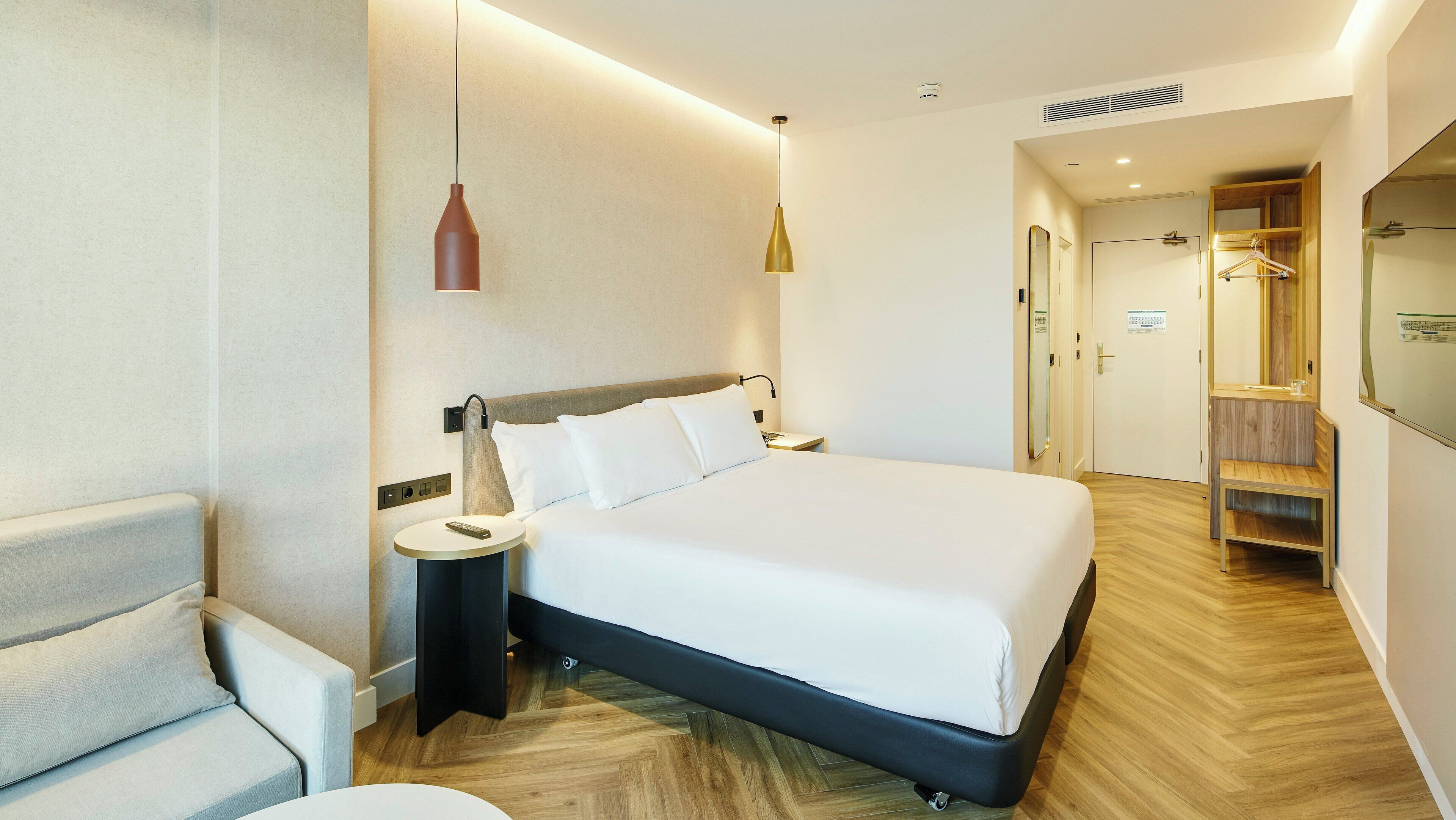 Une chambre d’hôtel moderne avec un grand lit, des tables de chevet, un luminaire suspendu et un dressing.